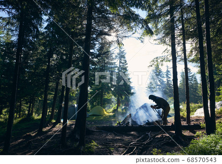 Tourist making fire near tents in forest. Tourist making fire near tents in forest. 68570543