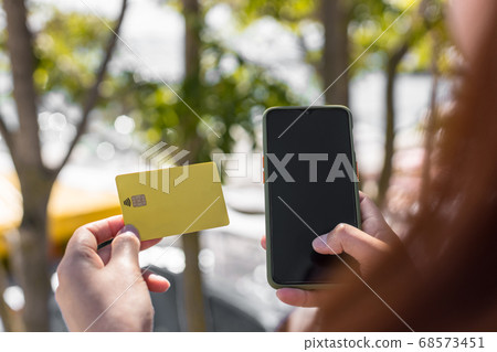 Beautiful young woman holding a credit card using mobile phone on the street. Online shopping concept Beautiful young woman holding a credit card using mobile phone on the street. Online shopping concept 68573451