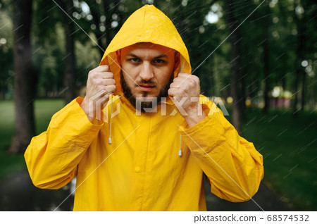 Man in raincoat puts on a hood in rainy day 68574532