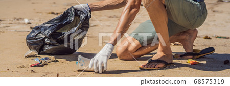 Man in gloves pick up plastic bags that pollute sea. Problem of spilled rubbish trash garbage on the beach sand caused by man-made pollution and environmental, campaign to clean volunteer in concept Man in gloves pick up plastic bags that pollute sea. Problem of spilled rubbish trash garbage on the beach sand caused by man-made pollution and environmental, campaign to clean volunteer in concept 68575319