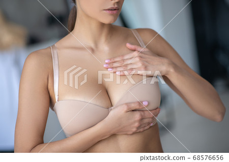 Woman in beige brassier examining her breast Woman in beige brassier examining her breast 68576656