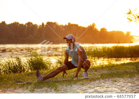 A young athletic man working out listening to the music at the riverside outdoors 68577057