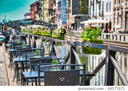 Lovely, romantic restaurant with blooming colorful flowers in pots on the side of Naviglio Grand canal in Milan Lovely, romantic restaurant with blooming colorful flowers in pots on the side of Naviglio Grand canal in Milan 68577872