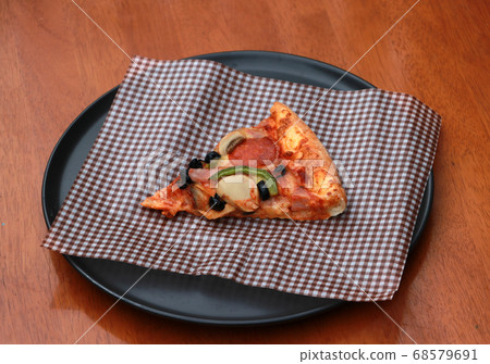 A piece of triangle Pizza  place on brown scotch paper  in the black round plate 68579691