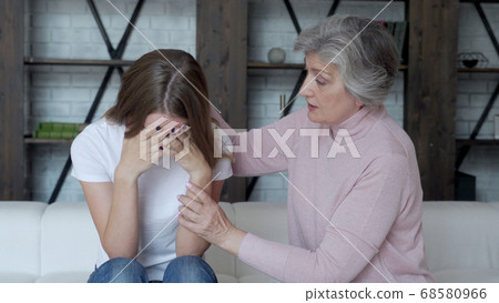 A middle aged mother and an adult daughter are sitting on the sofa. Mom calms her daughter, helps her through a bad divorce to break up with her boyfriend A middle aged mother and an adult daughter are sitting on the sofa. Mom calms her daughter, helps her through a bad divorce to break up with her boyfriend 68580966