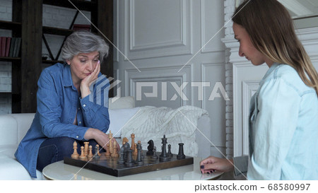 Mother and daughter play chess sitting on the sofa in the living room Mother and daughter play chess sitting on the sofa in the living room 68580997