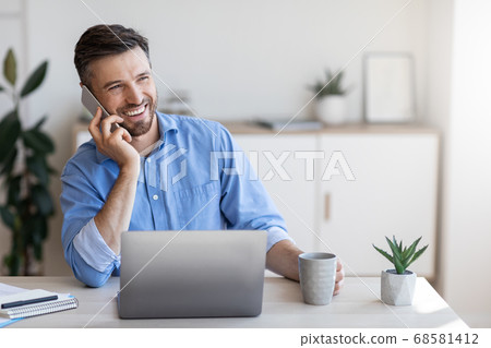 Smiling Male Office Employee Talking On Cellphone And Drinking Coffee At Workplace Smiling Male Office Employee Talking On Cellphone And Drinking Coffee At Workplace 68581412
