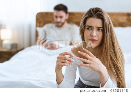 Sad wife takes off her wedding ring close up, husband typing on phone in bed Sad wife takes off her wedding ring close up, husband typing on phone in bed 68581548