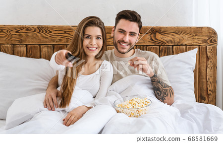 Entertainment in evening. Smiling man eating popcorn, woman presses button on remote control Entertainment in evening. Smiling man eating popcorn, woman presses button on remote control 68581669