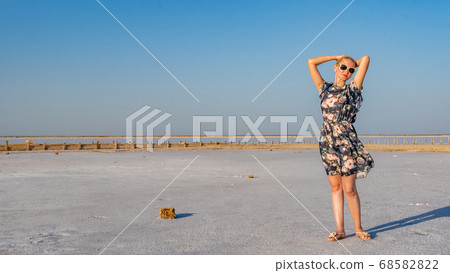 Cheerful girl in a beautiful dress with a kind look on a salty background like in winter on a lake with blue clouds in hot sunny weather Cheerful girl in a beautiful dress with a kind look on a salty background like in winter on a lake with blue clouds in hot sunny weather 68582822