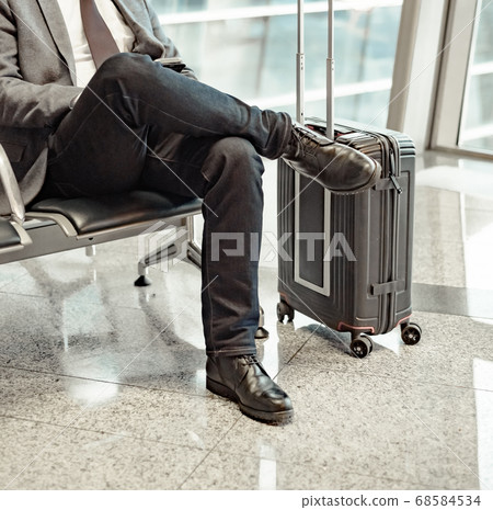 man waiting for his flight at the airport and looking at a mobile phone man waiting for his flight at the airport and looking at a mobile phone 68584534