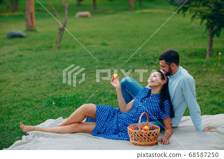 Young adult woman and man couple picnic sitting at green grass meadow in park. Young adult woman and man couple picnic sitting at green grass meadow in park. 68587250
