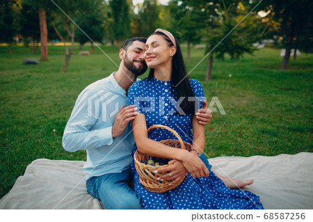 Young adult woman and man couple picnic sitting at green grass meadow in park. Young adult woman and man couple picnic sitting at green grass meadow in park. 68587256