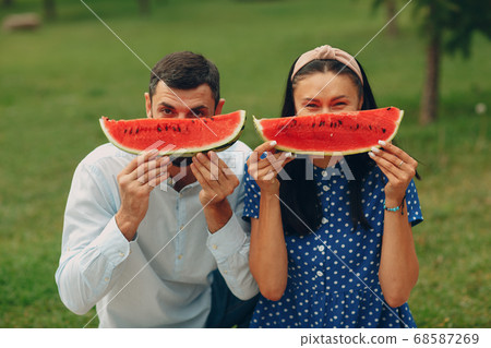 Young adult woman and man couple picnic at green grass meadow in park having fun and smile with watermelon Young adult woman and man couple picnic at green grass meadow in park having fun and smile with watermelon 68587269