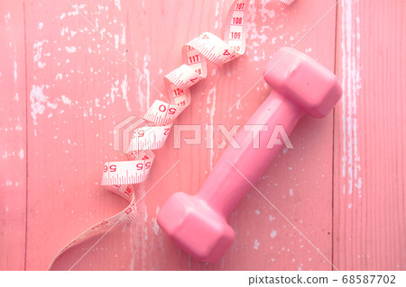 Fitness concept with dumbbell and measurement tape on pink Fitness concept with dumbbell and measurement tape on pink 68587702