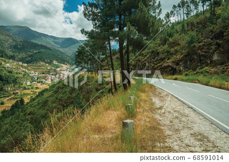 Road passing through hilly landscape and a village 68591014