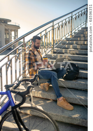 Man with laptop and coffee sitting on stairs near bike Man with laptop and coffee sitting on stairs near bike 68596351