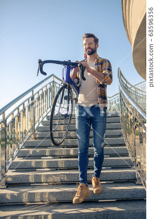 Energetic smiling man carrying bike down stairs Energetic smiling man carrying bike down stairs 68596356
