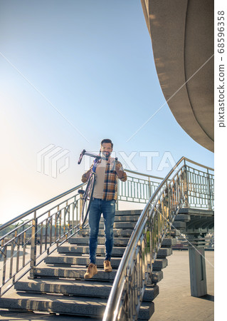 Smiling man carrying bike down city stairs Smiling man carrying bike down city stairs 68596358