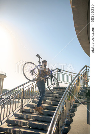 Young man carrying bicycle up the steps Young man carrying bicycle up the steps 68596359