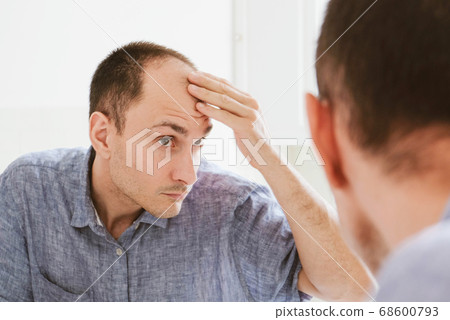 Young man looking at mirror worry about balding. Young man looking at mirror worry about balding. 68600793