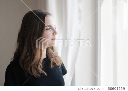 Portrait of young beautiful woman in black T-shirt by the window. Sad, pensive girl is lost in her thoughts. Mindfulness concept. Portrait of young beautiful woman in black T-shirt by the window. Sad, pensive girl is lost in her thoughts. Mindfulness concept. 68601239