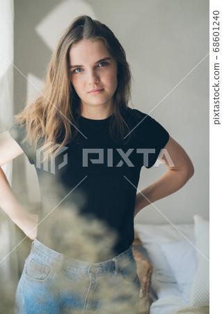Portrait of young beautiful woman in black T-shirt by the window through white flowers. Sad, pensive girl is lost in her thoughts. Mindfulness concept. Portrait of young beautiful woman in black T-shirt by the window through white flowers. Sad, pensive girl is lost in her thoughts. Mindfulness concept. 68601240