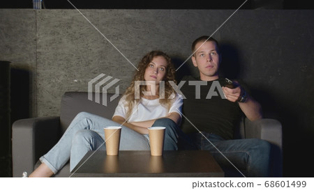 A young couple of millennials sits on the couch in front of the TV A young couple of millennials sits on the couch in front of the TV 68601499