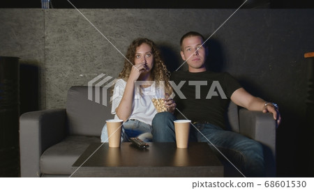 Beautiful girl and a young man sitting on the couch and watch TV. People relax on the couch. Beautiful girl and a young man sitting on the couch and watch TV. People relax on the couch. 68601530