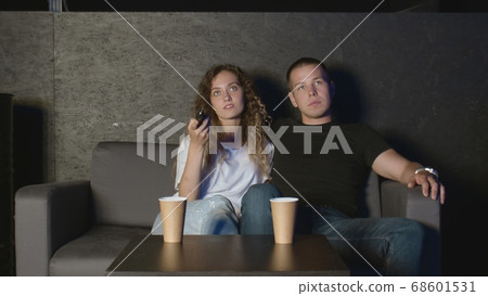 Beautiful girl and a young man sitting on the couch and watch TV. People relax on the couch. Beautiful girl and a young man sitting on the couch and watch TV. People relax on the couch. 68601531