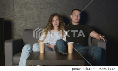 Beautiful girl and a young man sitting on the couch and watch TV. People relax on the couch. Beautiful girl and a young man sitting on the couch and watch TV. People relax on the couch. 68601532