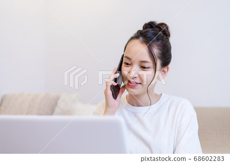 一個女人在家裡看一台個人計算機時在智能手機上聊天 68602283