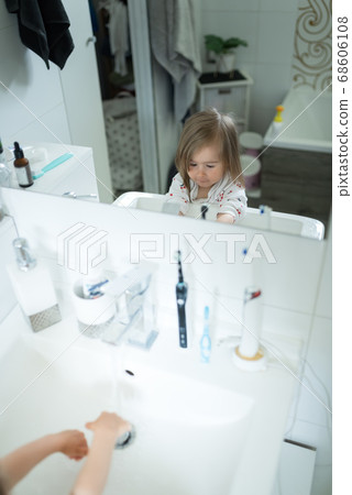 Cute little girl 2-3 years old washing hands with soap and water in bright bathroom. Mirror reflection Cute little girl 2-3 years old washing hands with soap and water in bright bathroom. Mirror reflection 68606108
