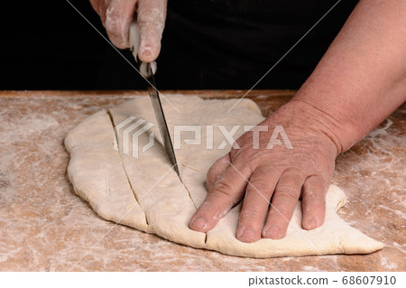 The cook slicers raw dough with a knife on a 68607910