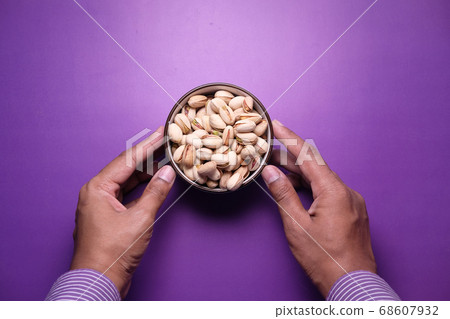 man hand holding a bowl salted pistachios nut on purple background man hand holding a bowl salted pistachios nut on purple background 68607932