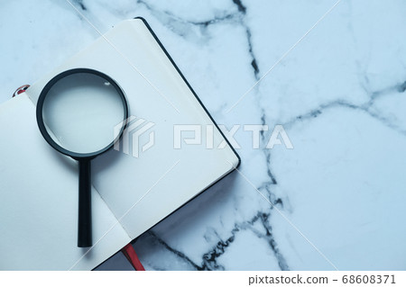 open book and magnifying glass on table. 68608371