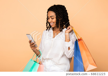 Happy African Girl Using Cellphone Holding Shopper Bags, Studio Shot Happy African Girl Using Cellphone Holding Shopper Bags, Studio Shot 68611223
