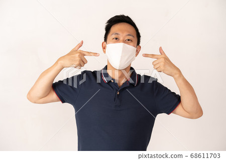 Asian man wearing face mask with hands pointing at face 68611703