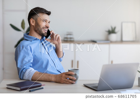 Smiling young businessman having coffee break at workplace and talking on cellphone 68611705