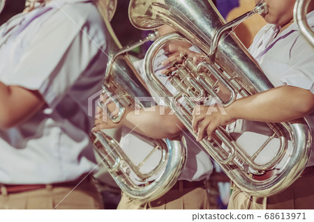 Male student with friends blow the euphonium with the band for performance on stage at night. 68613971