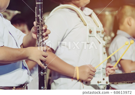 Male student with friends blow the clarinet with the band for performance on stage at night. 68613972