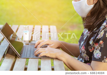 A quarantine woman wear a protective mask to prevent the spread of of the Corona virus (Covid-19) ,Use a laptop to work from home with green lawn and garden. New normal concept.Selective focus A quarantine woman wear a protective mask to prevent the spread of of the Corona virus (Covid-19) ,Use a laptop to work from home with green lawn and garden. New normal concept.Selective focus 68614084