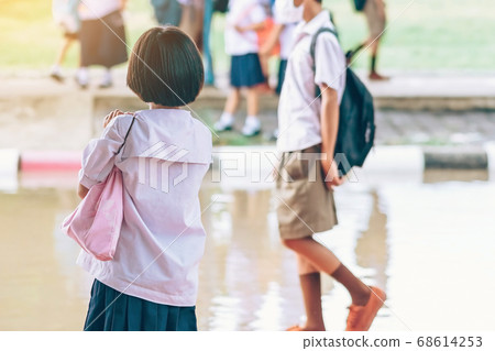 Female elementary school student wear face mask to prevent the Coronavirus(Covid-19) wait for her parents to pick her up to return home after school and the rain just stop in front of the school gate Female elementary school student wear face mask to prevent the Coronavirus(Covid-19) wait for her parents to pick her up to return home after school and the rain just stop in front of the school gate 68614253