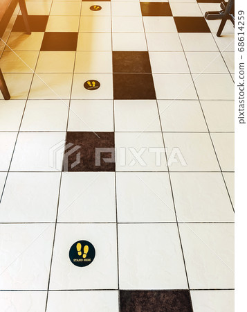 STAND HERE foot sign or symbol on the wooden floor in coffee shop. Coffee shop set foot sign for social distancing to order coffee and wait to take home. STAND HERE foot sign or symbol on the wooden floor in coffee shop. Coffee shop set foot sign for social distancing to order coffee and wait to take home. 68614259