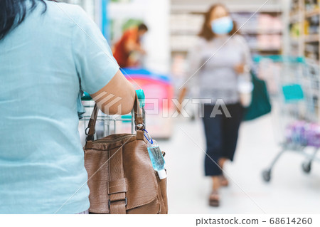 Mini portable alcohol gel bottle to kill Corona Virus(Covid-19) hang on a leather shoulder bag of a woman wearing a mask to shopping in supermarket.New normal lifestyle.Selective focus on alcohol gel Mini portable alcohol gel bottle to kill Corona Virus(Covid-19) hang on a leather shoulder bag of a woman wearing a mask to shopping in supermarket.New normal lifestyle.Selective focus on alcohol gel 68614260