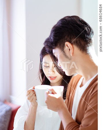Young asian woman and man are enjoying spending time together at home with cup of coffee in hands. Young asian woman and man are enjoying spending time together at home with cup of coffee in hands. 68614684