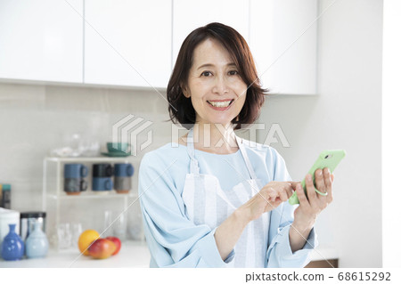 A middle-aged woman looking at a smartphone in the kitchen A middle-aged woman looking at a smartphone in the kitchen 68615292