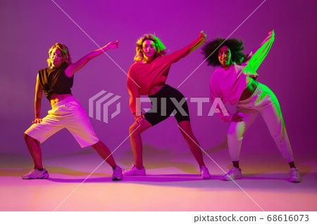 Sportive girls dancing hip-hop in stylish clothes on gradient background at dance hall in neon light 68616073