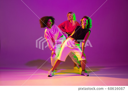Sportive girls dancing hip-hop in stylish clothes on gradient background at dance hall in neon light 68616087