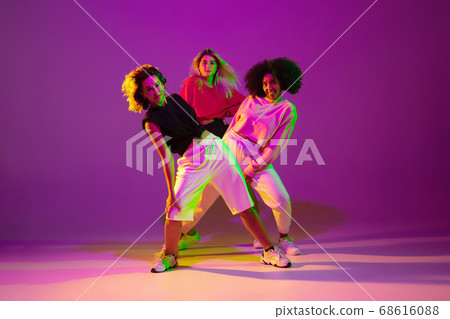 Sportive girls dancing hip-hop in stylish clothes on gradient background at dance hall in neon light 68616088